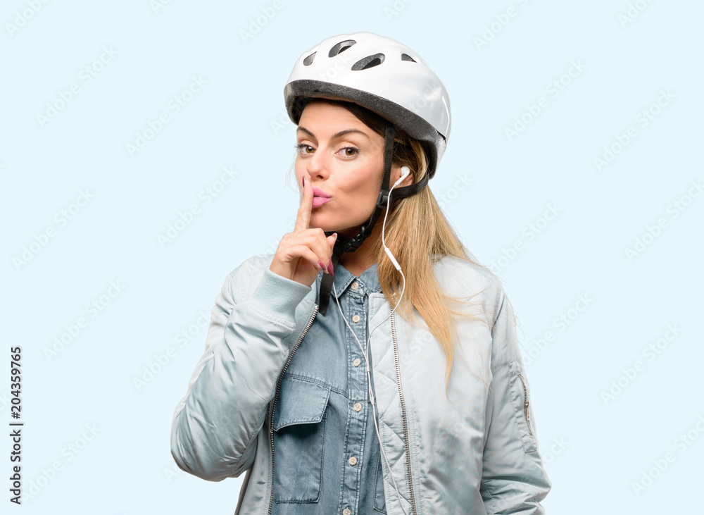 Young woman with bike helmet and earphones with index finger on lips, ask to be quiet. Silence and secret concept Young woman with bike helmet and earphones with index finger on lips, ask to be quiet. Silence and secret concept