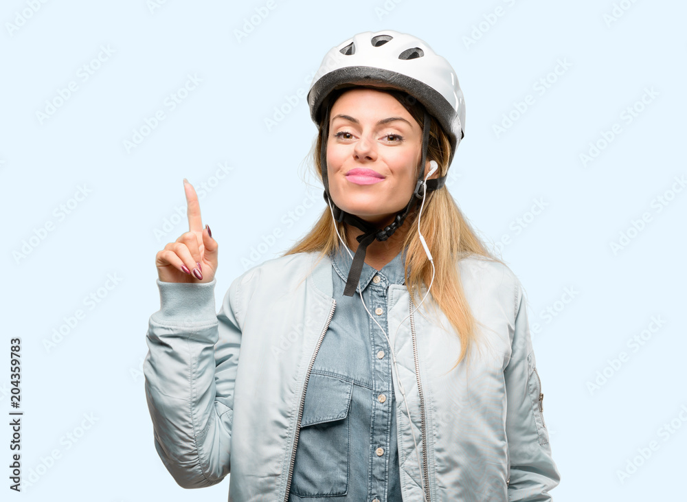 Young woman with bike helmet and earphones raising finger, the number one Young woman with bike helmet and earphones raising finger, the number one