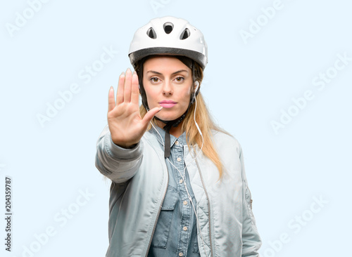 Young woman with bike helmet and earphones annoyed with bad attitude making stop sign with hand, saying no, expressing security, defense or restriction, maybe pushing © Krakenimages.com