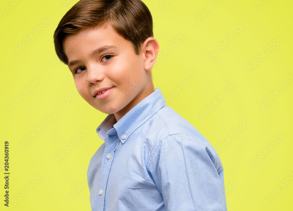 Handsome toddler child with green eyes confident and happy with a big natural smile laughing over yellow background Handsome toddler child with green eyes confident and happy with a big natural smile laughing over yellow background