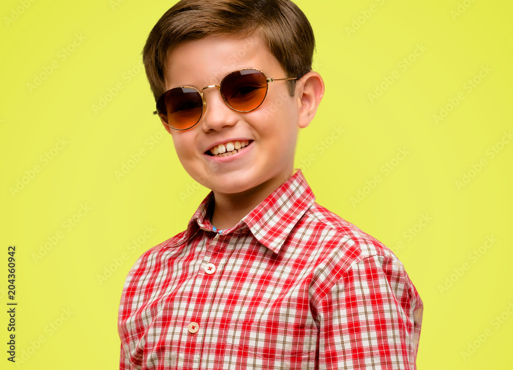 Handsome toddler child with green eyes confident and happy with a big crazy smile laughing over yellow background Handsome toddler child with green eyes confident and happy with a big crazy smile laughing over yellow background