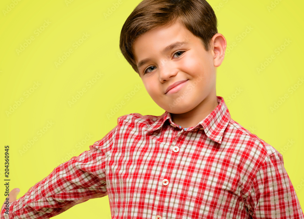 Handsome toddler child with green eyes confident and happy with a big natural smile inviting to enter over yellow background