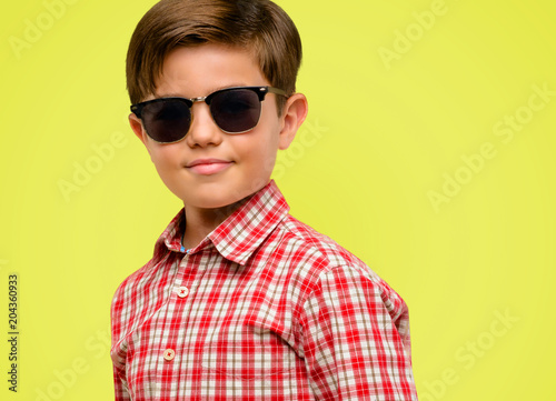 Handsome toddler child with green eyes confident and happy with a big natural smile looking at camera over yellow background