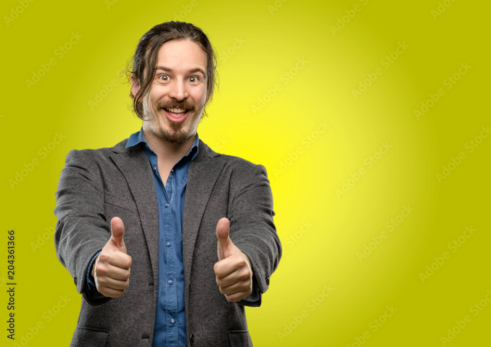 Handsome young man stand happy and positive with thumbs up approving with a big smile expressing okay gesture Handsome young man stand happy and positive with thumbs up approving with a big smile expressing okay gesture