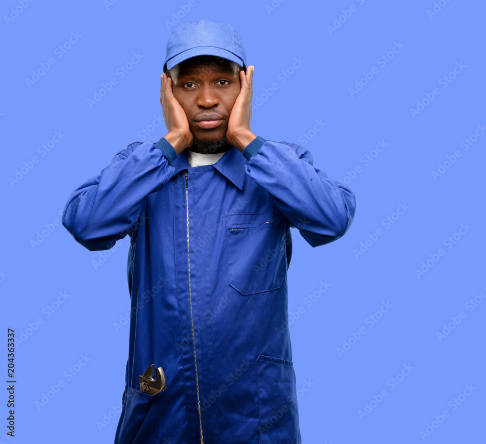 African black plumber man covering ears ignoring annoying loud noise, plugs ears to avoid hearing sound. Noisy music is a problem. African black plumber man covering ears ignoring annoying loud noise, plugs ears to avoid hearing sound. Noisy music is a problem.
