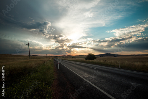 Fotografie Road stretching into the horizon across vast grassy plains with spectacular sky