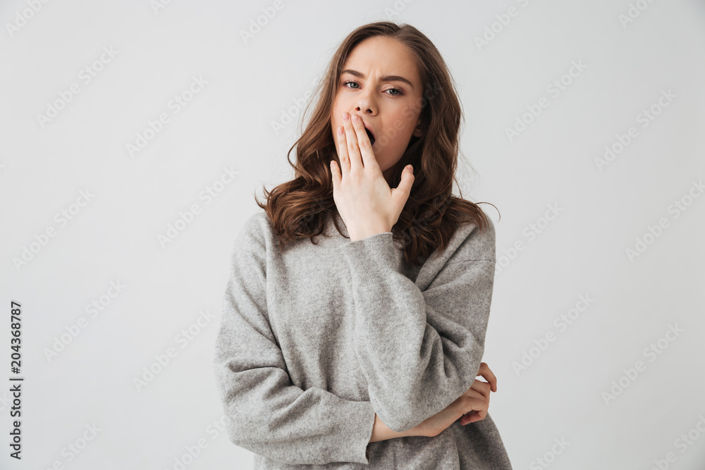 Tired brunette woman in sweater yawns and covering her mouth Tired brunette woman in sweater yawns and covering her mouth