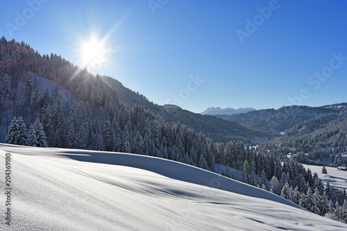 Deeply snow-covered landscape in the Allgaeu Alps with forests and the sun at a beautiful winter day. Bavaria, Germany