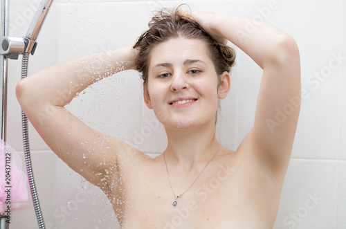 Beautiful brunette woman washing hair in shower at morning