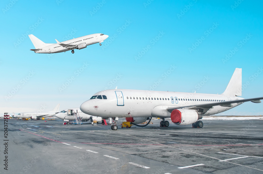 Passenger aircraft row, airplane parked on service before departure at the airport. One aircraft take off to runway in the cloudy sky. Passenger aircraft row, airplane parked on service before departure at the airport. One aircraft take off to runway in the cloudy sky.