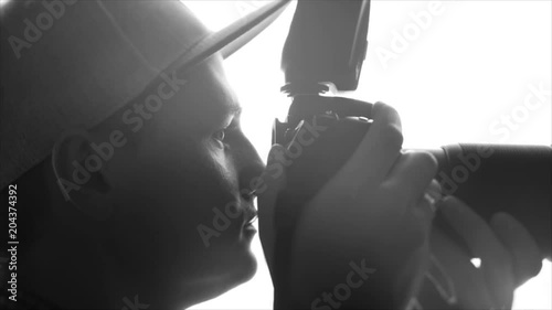 Young male photographer taking pictures with professional camera. Close-up of black and white silhouette of a young male photographer in cap taking pictures with a professional camera. Slow motion.