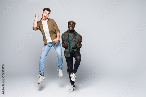 Portrait of a two mixed race cheerful young men jumping and celebrating isolated over white background