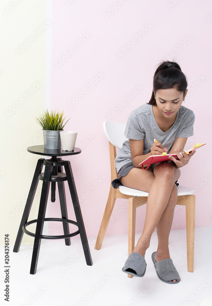 The beauty lady is sitting on chair and writing on book,pastel wallpaper