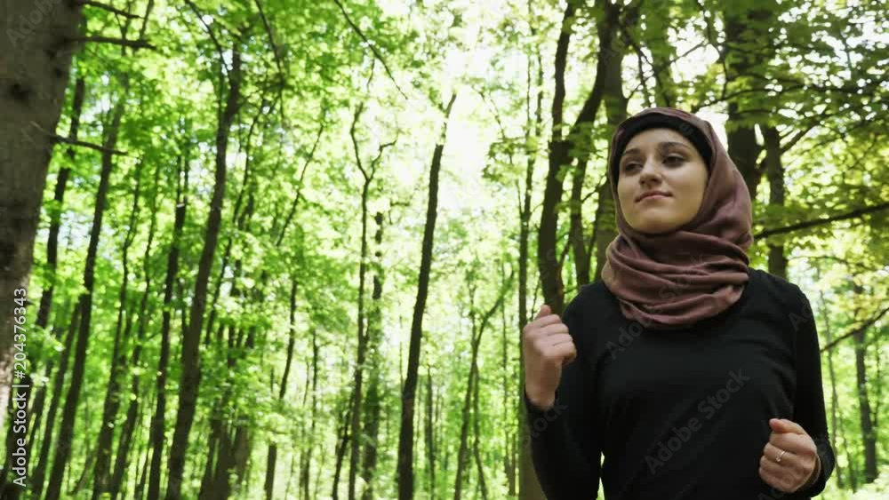 Young athletic girl in hijab running, jogging in green park, forest, front side view 50 fps Young athletic girl in hijab running, jogging in green park, forest, front side view 50 fps