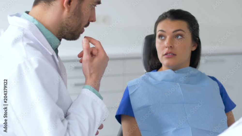medicine, dentistry and healthcare concept - male dentist talking to female patient at dental clinic office medicine, dentistry and healthcare concept - male dentist talking to female patient at dental clinic office