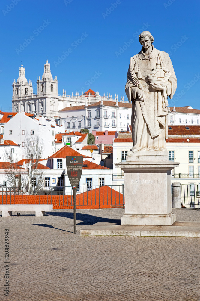 Fototapeta premium Lisbon, Portugal - December 10, 2013: Sao Vicente Statue (St. Vincent of Saragossa - patron saint of Lisbon) in Miradouro das Portas do Sol viewpoint, Sao Vicente de Fora Monastery and Alfama rooftops