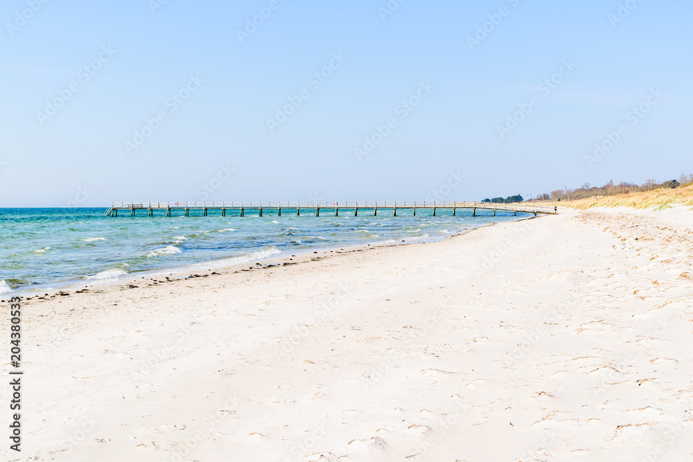Falsterbo, Sweden - Long wooden pier on a sandy beach. Person visible walking by the pier.