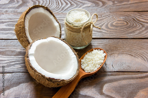 fresh coconut cracked in half on a wooden table with coconut chips in a glass jar and in a wooden spoon with a place for writing