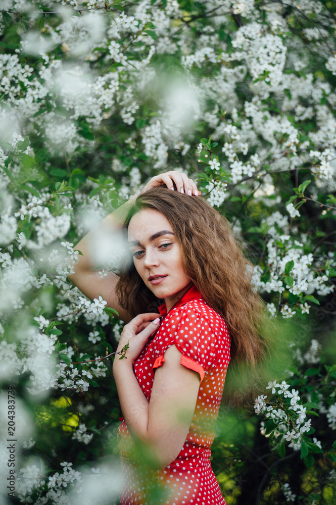A beautiful girl in a dress stands next to a blooming cherry bush. A beautiful girl in a dress stands next to a blooming cherry bush.
