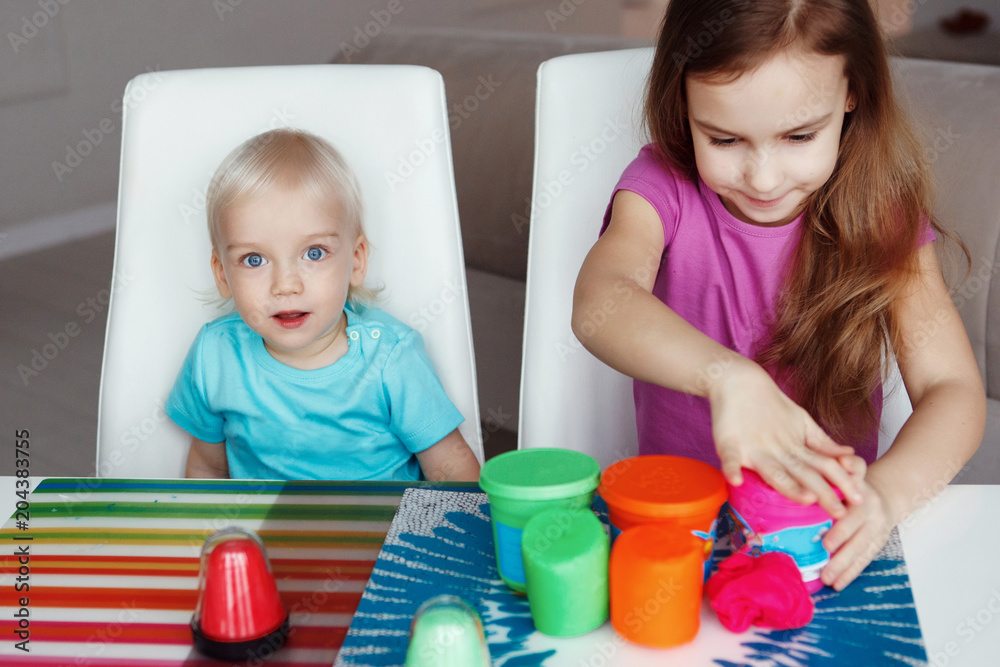 Two happy children Blond boy and girl playing sitting at table at home Two happy children Blond boy and girl playing sitting at table at home