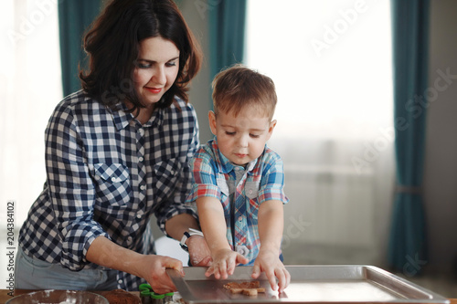 Mother and son dressed in plaid shirts are cooked in the kitchen of flour and dough