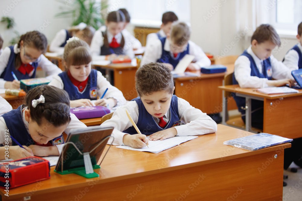 Pupils at the desk think and decide the task in the school. Primary education, training and people concept