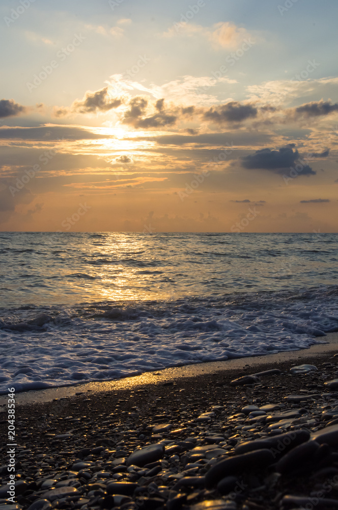 Amazing sea sunset on the pebble beach, the sun, waves, clouds Amazing sea sunset on the pebble beach, the sun, waves, clouds