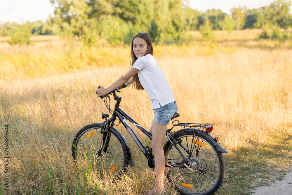 Beautiful brunette girl riding mountain bike in field at sunset