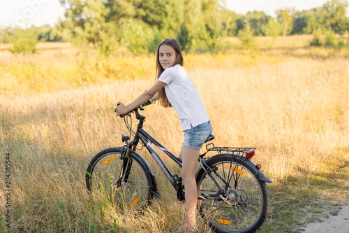 Beautiful brunette girl riding mountain bike in field at sunset