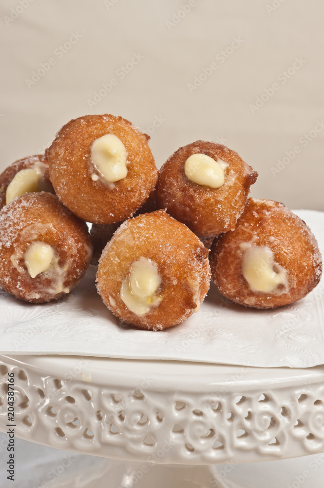 Front view, close up of five freshly baked, homemade lemon cream filled donuts on a white, round, display dish