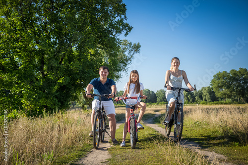 Happy smiling family riding bicycles on countryside road