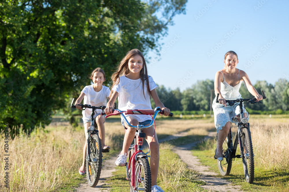 Portrait of three happy girls riding bicycles in field at sunny day