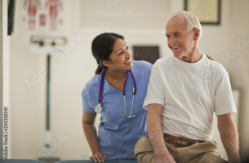 Smiling female nurse comforting an elderly male patient inside an exam room.