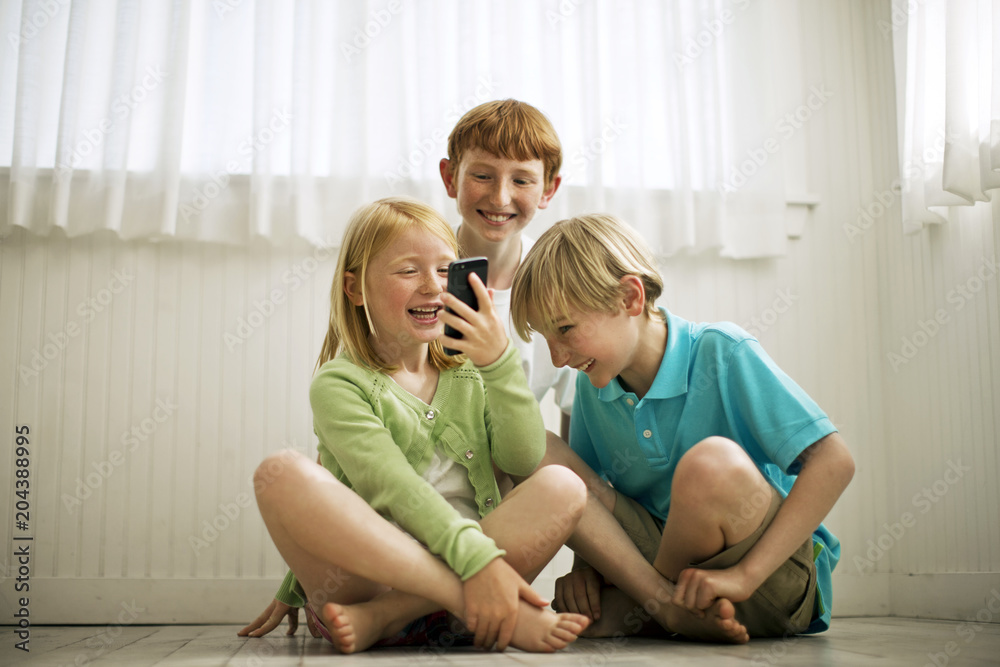 Smiling siblings playing with smartphone at home