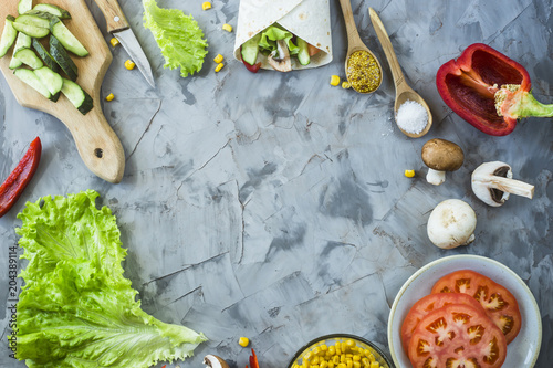 Cooking Mexican vegan burrito - vegetables and mushrooms and a prepared dish on a gray kitchen table. Top view, copyspace