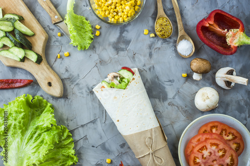 Vegan burrito from vegetables, mushrooms and tortillas. On a gray table among the ingredients. Top view