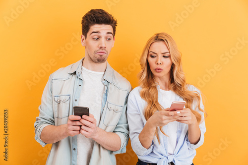 Fotografía Photo of serious man and woman in casual wear peeking at each others mobile phon