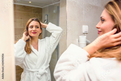 Beautiful woman wearing bathrobe looking herself in a mirror in a bathroom