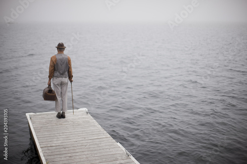 Mature man wearing a hat and carrying a leather bag standing at the end of a jetty facing towards the open sea. photo