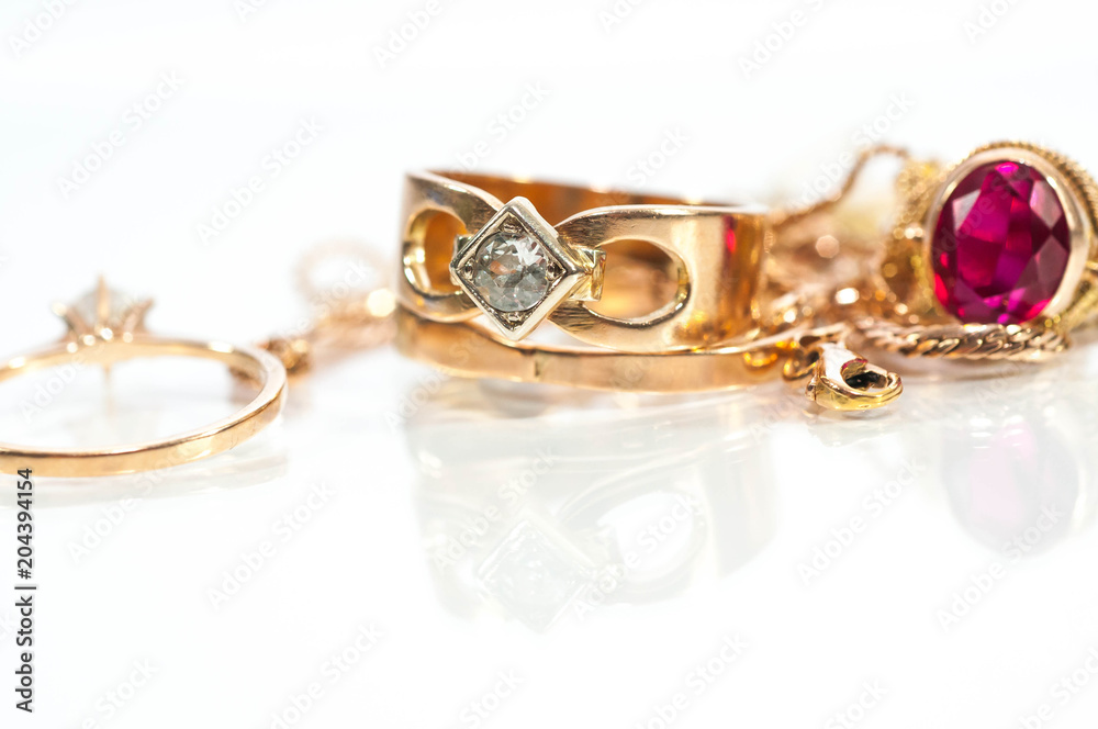 Real gold rings, chains, diamonds and gems on shiny surface, white background. Real gold rings, chains, diamonds and gems on shiny surface, white background.
