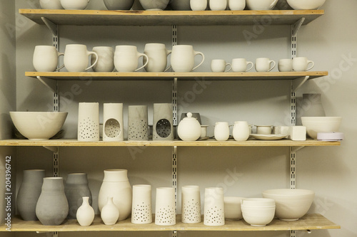 Racks of hand thrown hand crafted pottery vases and objects on shelves in the drying room. 