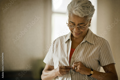Woman looking down as she buttons up her shirt.