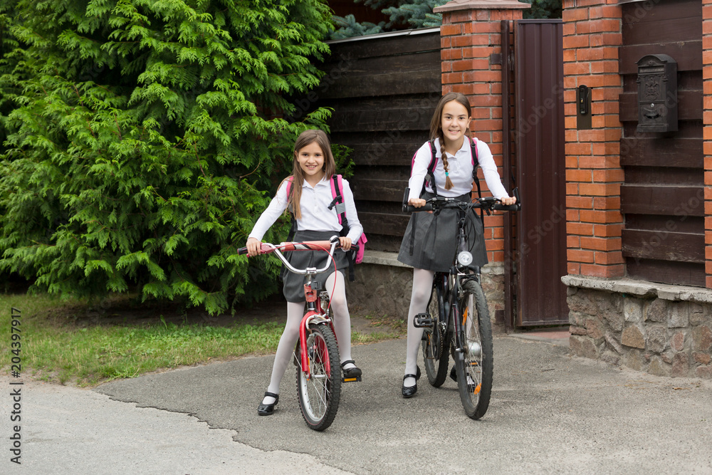 Fototapeta premium Two smiling girls in school uniform riding to school on bicycles