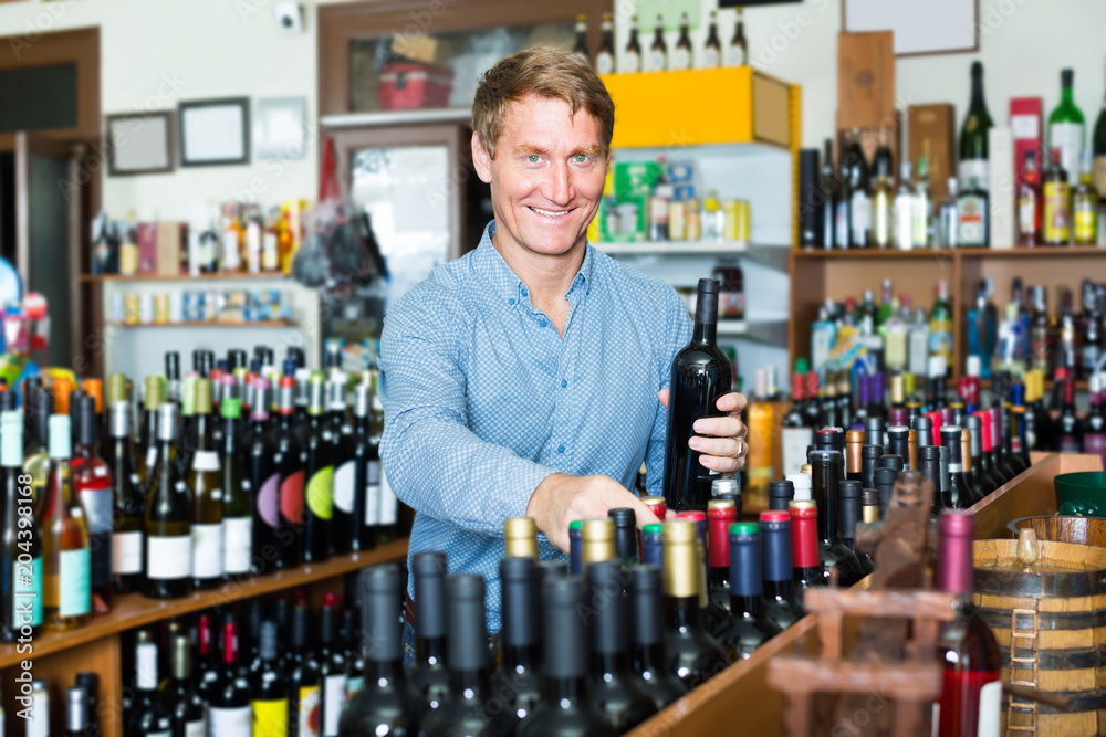 Smiling middle-aged man customer buying bottle of wine