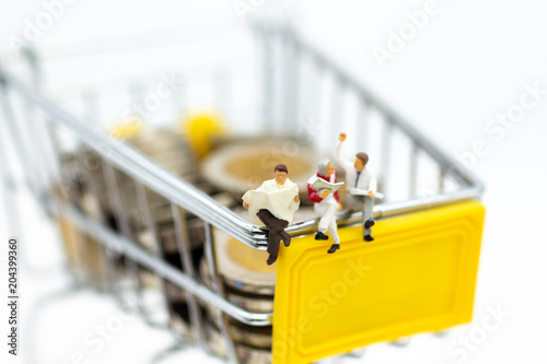 Miniature people : Businessman reading on shopping cart on stack of coin. Image use for retail business concept.