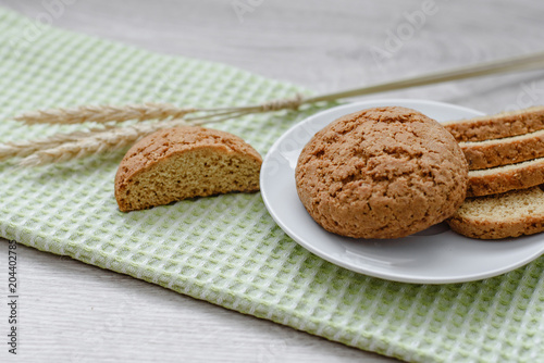 Homemade cookies on a white saucer and green napkins, spikelets of wheat on a wooden background photo