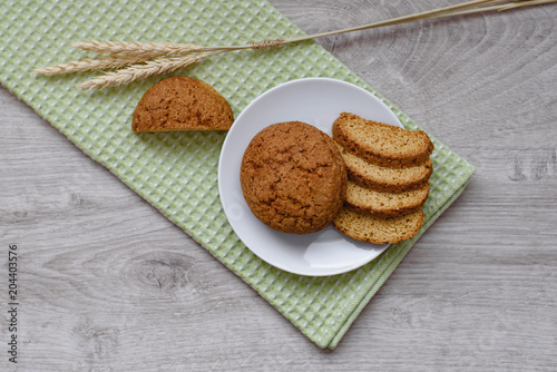 Homemade cookies on a white saucer and green napkins, spikelets of wheat on a wooden background photo