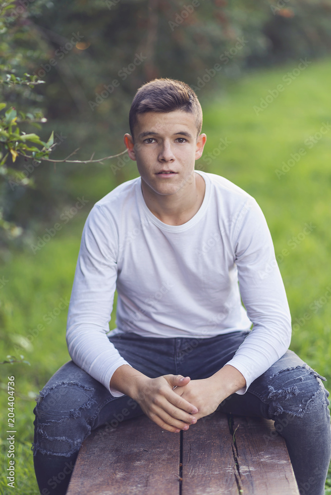 Stylish teenager sitting on a wooden bench on a city park Stylish teenager sitting on a wooden bench on a city park