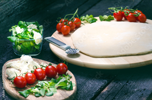 Italian food, cuisine. Margherita pizza on a black, wooden table with igredients like tomatoes, salad, cheese, mozzarella, basil. Delicious homemade food.  photo