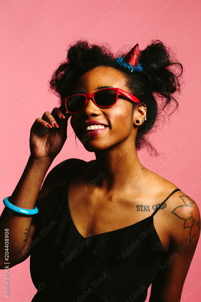 Portrait of a cool party girl with sunglasses and party hat, isolated on pink studio background Portrait of a cool party girl with sunglasses and party hat, isolated on pink studio background